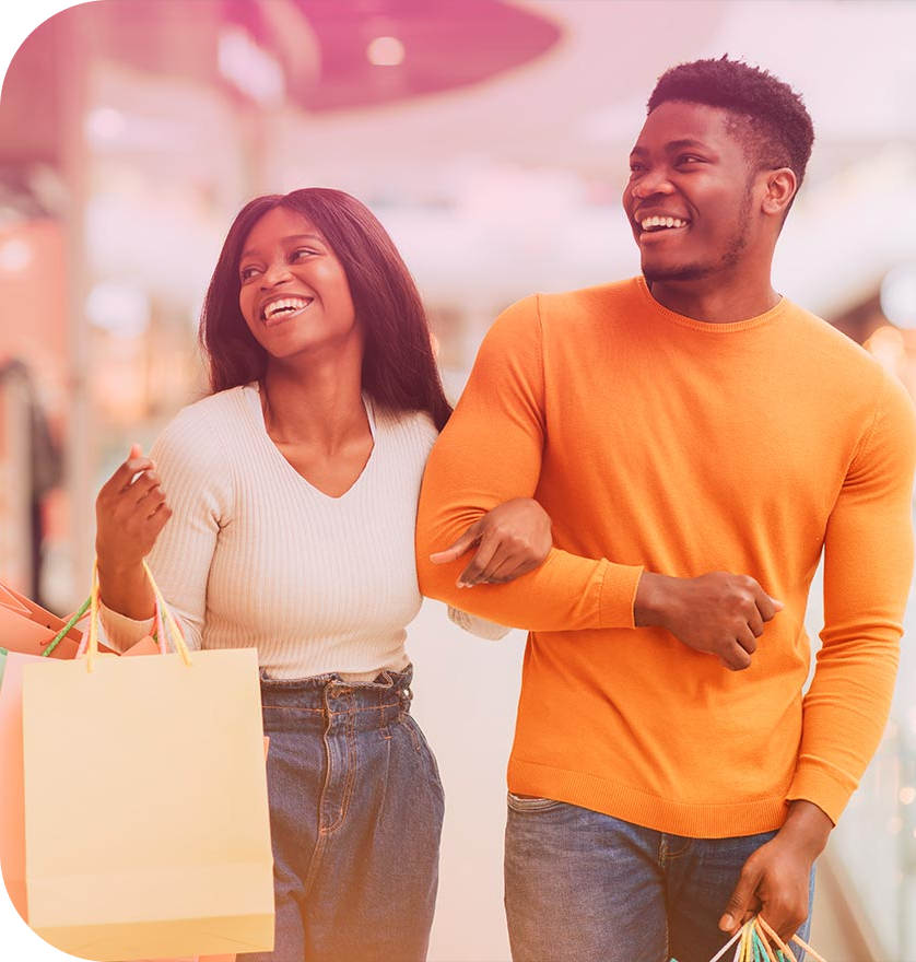 Mulher e homem com os braços entrelaçados, os dois estão sorrindo e segurando compras com os braços livres